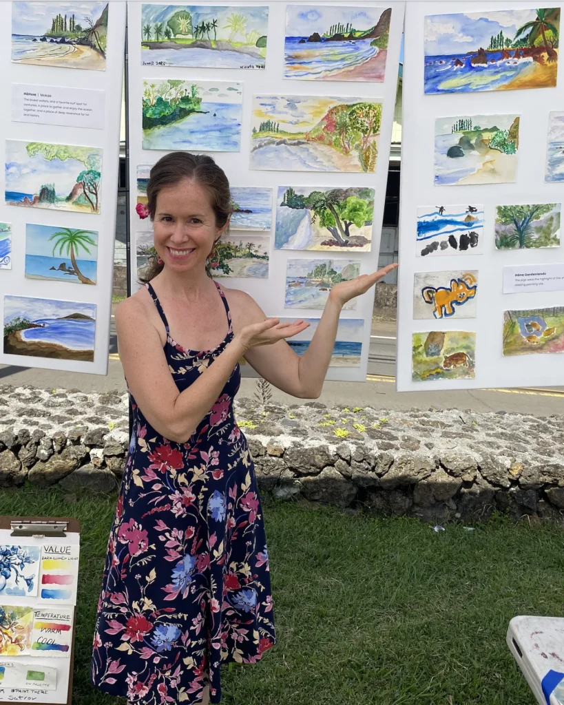 Elizabeth Blue smiling beside a display of her watercolor paintings