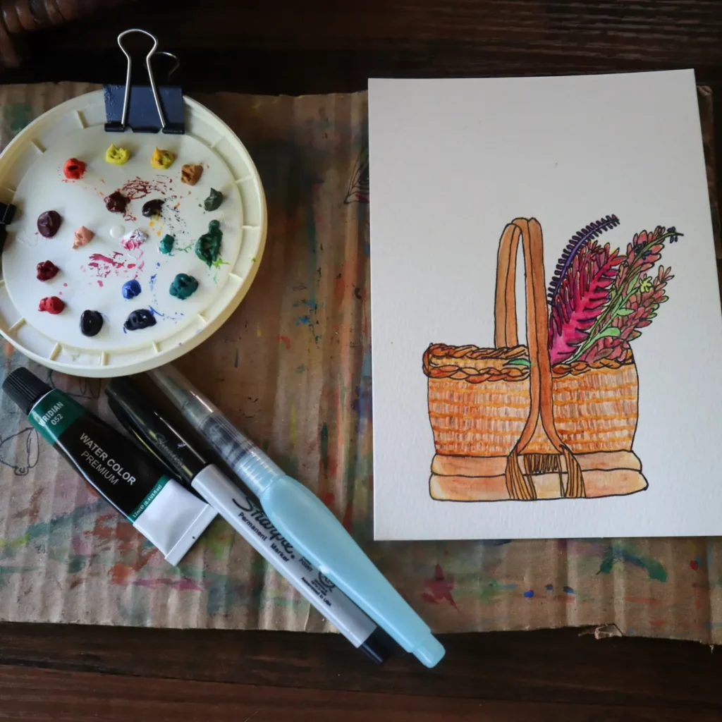 Elizabeth's watercolor of a woven basket of flowers, beside her paint palette, a Sharpie and a water brush